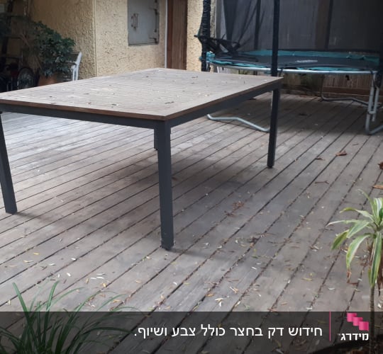 שולחן עץ על דק עץ בגינה עם צמחייה מסביב